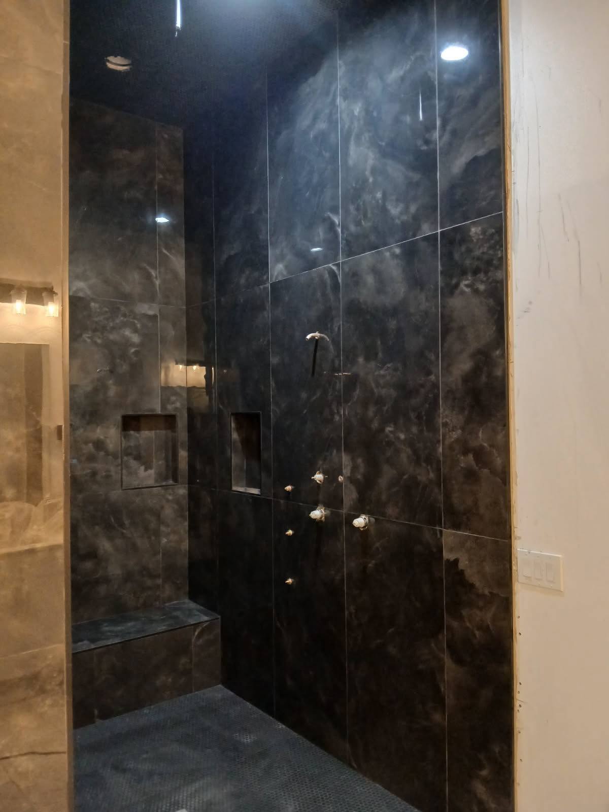 Dramatic black marble shower with recessed niches and bench